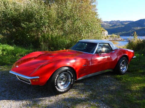 Voiture de sport rouge garée près d'un lac, entourée de verdure et de montagnes en Norvège.