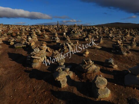 Des cairns de pierres s'étendent sur le sol, en Norvège. Le ciel est partiellement nuageux, avec des ombres projetées sur le terrain.