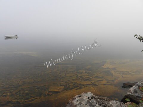 Eau calme avec un bateau sur un lac en Norvège, entouré de brume et de rochers.