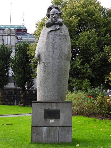 Statue d'Henrik Ibsen dans un parc à Bergen, Norvège, entourée de verdure et de fleurs.