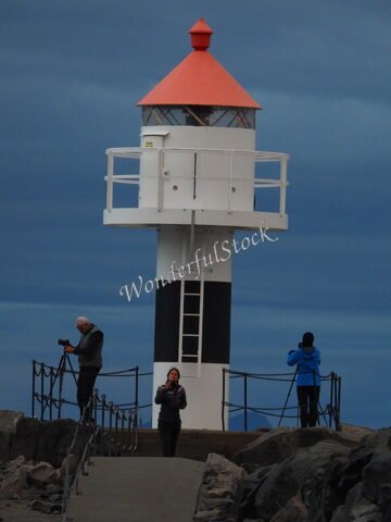 Phare avec un toit rouge et trois personnes sur un chemin de pierre, Norvège.
