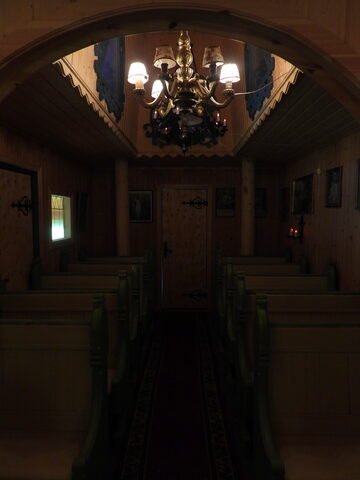 Intérieur d'une stavkirke à Savjord, Norvège, avec des bancs en bois, un lustre doré et des portraits accrochés aux murs.