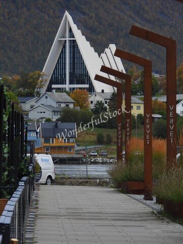 Édifice moderne avec un toit en forme de pyramide à Tromsø, Norvège, entouré de maisons colorées et d'une allée pavée.