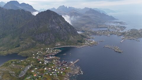 Vue aérienne d'une petite ville côtière entourée de montagnes en Norvège. Des maisons colorées bordent le rivage et des eaux calmes.