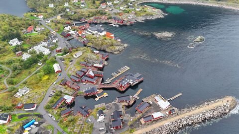 Vue aérienne d'un village côtier avec des maisons rouges en Norvège. Le paysage présente des rochers et des bateaux dans l'eau.