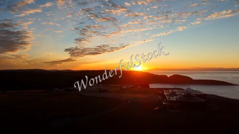 Coucher de soleil sur le Cap Nord en Norvège, avec des nuages et un bâtiment en premier plan près de l'océan.