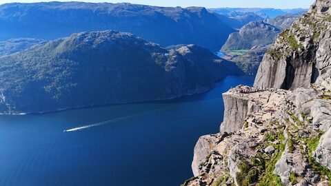 Vue aérienne de Preikestolen en Norvège, avec des randonneurs sur la falaise et un fjord en contrebas.