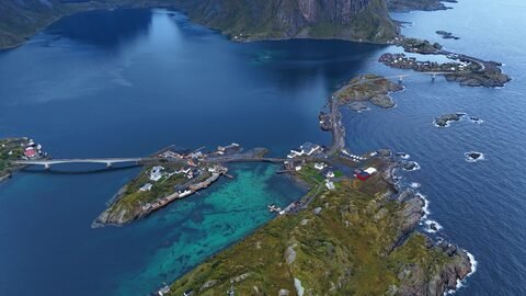 Vue aérienne d'une petite localité côtière en Norvège, avec des maisons colorées et des eaux turquoise.