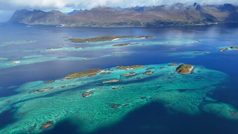 Vue aérienne des îles et des eaux turquoise de Senja, en Norvège, avec des montagnes en arrière-plan.