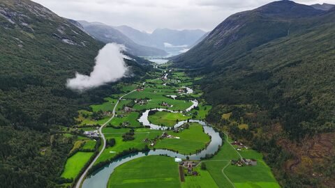Vallée verdoyante avec des fermes et une rivière sinueuse à Stryn, Norvège. Montagnes en arrière-plan et nuages bas.