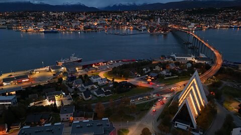 Vue aérienne de Tromsø, Norvège, avec des bâtiments illuminés et un pont traversant un fjord.