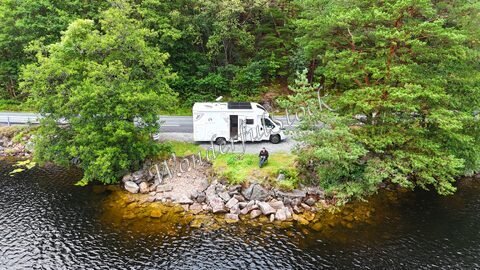 Camion aménagé stationné au bord d'un lac entouré d'arbres en Norvège.