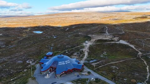 Centre du cercle arctique en Norvège, bâtiment distinctif avec un toit bleu, entouré de paysages vallonnés et de lacs.