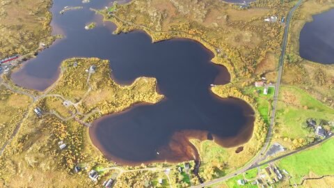 Lac entouré de terre et de maisons, en Norvège. Des zones boisées et des routes sont visibles autour du plan d'eau.