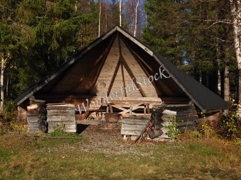 Un abri en bois avec un toit en pente, situé en Finlande, entouré d'arbres et d'herbe.