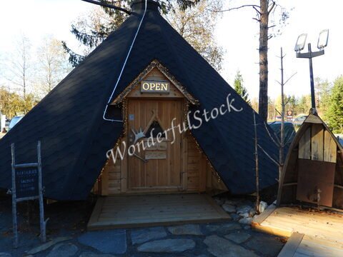 Cabane de style traditionnel avec un toit noir, située à Rovaniemi, Finlande, avec un panneau "OPEN" et des éléments en bois.