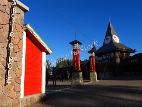 Arctic Circle à Rovaniemi, Finlande, avec des bâtiments en bois, des poteaux signalétiques rouges et un ciel bleu.