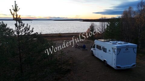 Un camping-car près d'un lac en Finlande, avec des arbres et un coucher de soleil en arrière-plan.
