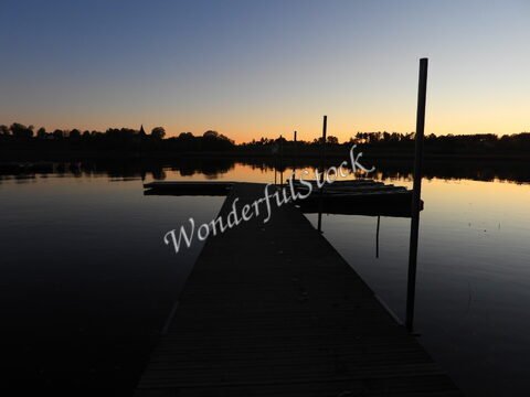 Un quai en bois au bord de l'eau à Hammarskog, Suède, avec des silhouettes de bateaux et un ciel crépusculaire.