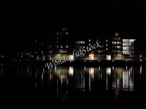 Bâtiments illuminés au bord de l'eau à Hudiksvall, Suède, avec des reflets sur la surface noire du lac.