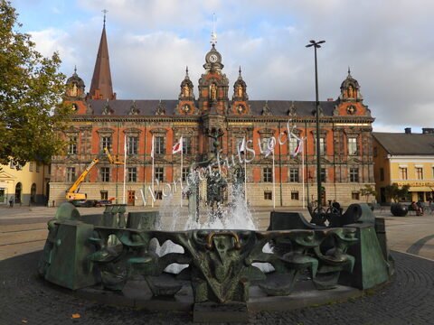 Fontaine au premier plan avec un bâtiment historique en briques rouges à Malmö, Suède.