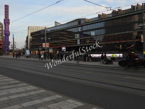 Des personnes marchent le long d'une rue avec des tramways à Stockholm, Suède, devant un bâtiment moderne avec des panneaux publicitaires.