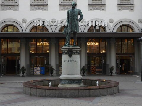 Statue de Nils Ericson devant la gare centrale à Stockholm, Suède, avec une fontaine circulaire et des plantes en pot.