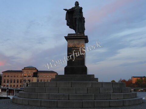 Statue de Karl XIV Johan à Stockholm, Suède, avec un bâtiment historique en arrière-plan et un ciel nuageux.