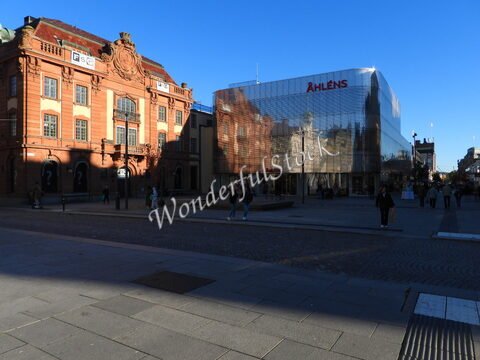Bâtiment historique et magasin moderne à Uppsala, Suède, avec des personnes marchant sur une rue pavée sous un ciel bleu.