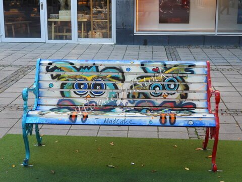 Banc coloré avec des dessins d'oiseaux à Uppsala, Suède, sur un sol pavé avec des éléments de verdure.