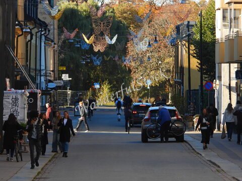 Rue animée à Uppsala, Suède, avec des personnes marchant et des décorations en forme de papillons suspendues.