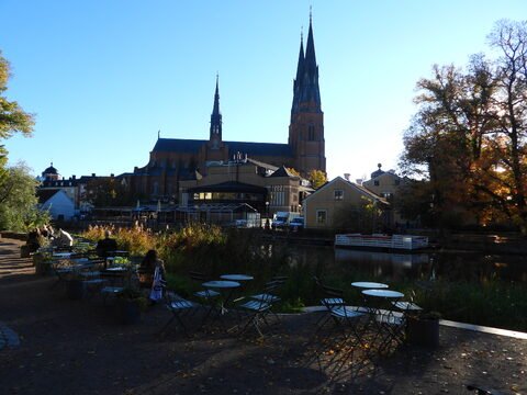 Église avec des flèches et terrasses près d'un canal à Uppsala, Suède, entourée d'arbres et de bâtiments colorés.