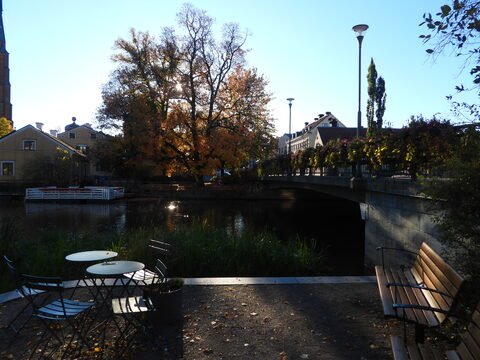 Un pont sur une rivière entouré d'arbres et de bâtiments, à Uppsala, Suède, avec des tables et des chaises au premier plan.