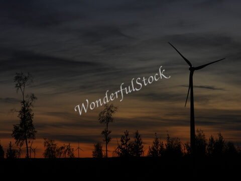 Éolienne silhouette au coucher de soleil, Suède. Des arbres se dressent en avant-plan, créant un contraste avec le ciel coloré.