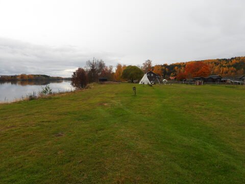 Un espace verdoyant avec un tipi, des maisons en bois et un lac, en Suède.