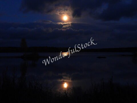 L'eau calme reflète la lune au-dessus d'un lac en Suède. Des nuages sombres entourent la scène, créant une ambiance nocturne.