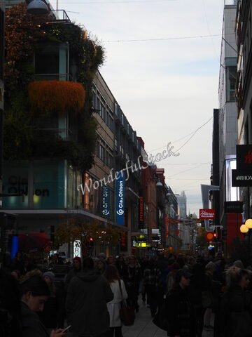 Rue animée à Stockholm, Suède, avec des boutiques et des panneaux lumineux, entourée de bâtiments modernes et d'une végétation sur façade.