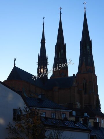Église avec trois flèches, Uppsala, Suède, entourée de bâtiments aux toits sombres sous un ciel clair.