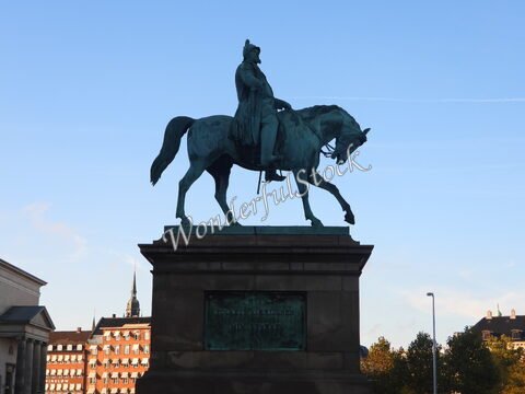 Statue équestre à Copenhague, Danemark, avec un ciel bleu et des bâtiments en arrière-plan.