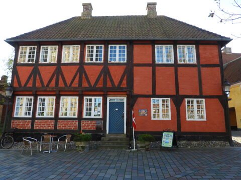 Maison à colombages rouge et noire à Ribe, Danemark, avec des fenêtres blanches et un drapeau danois sur le devant.