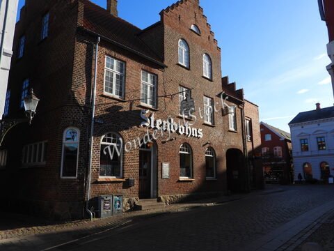 Bâtiment en briques avec l'inscription "Slenbahns" à Ribe, Danemark, sur une rue pavée, entouré de maisons colorées.