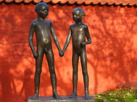 Deux statues d'enfants en bronze se tenant par la main, devant un mur en briques rouges, à Ribe, Danemark.