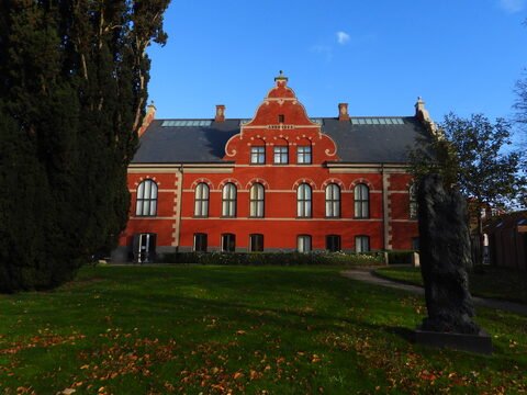 Bâtiment rouge avec des fenêtres arrondies à Ribe, Danemark, entouré d'arbres et de pelouse.