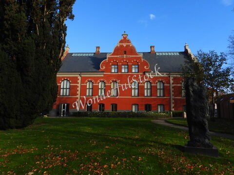 Bâtiment rouge avec des fenêtres arrondies à Ribe, Danemark, entouré d'arbres et de pelouse.