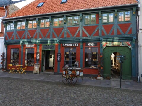 Bâtiment coloré avec des fenêtres à petits carreaux et un café à Ribe, Danemark, avec des tables jaunes à l'extérieur.