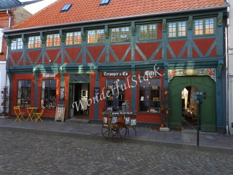 Bâtiment coloré avec des fenêtres à petits carreaux et un café à Ribe, Danemark, avec des tables jaunes à l'extérieur.