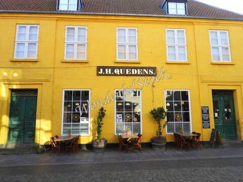 Façade d'un bâtiment jaune avec des chaises en bois à Ribe, Danemark. Des pots de fleurs sont visibles près des fenêtres et à l'extérieur.