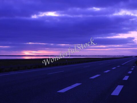 Coucher de soleil sur une route au Danemark, avec des nuages violets et un reflet sur l'eau.