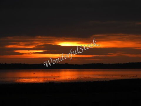 Coucher de soleil sur le lac à Rømø, Danemark, avec des reflets orange dans l'eau et des nuages sombres en arrière-plan.