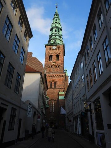 Tour de l'église dans une ruelle étroite à Copenhague, Danemark, avec un ciel partiellement nuageux et des bâtiments historiques de chaque côté.